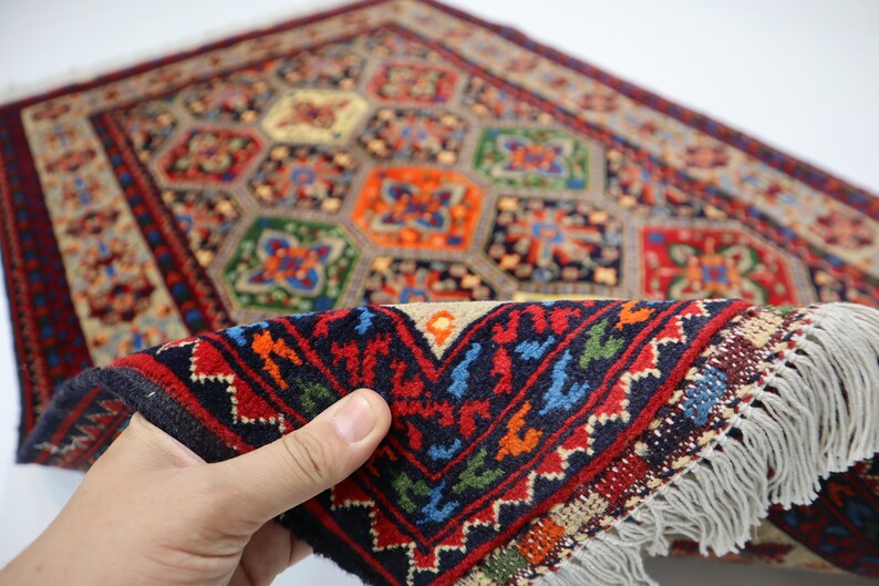 May include: A colourful hand-woven rug with a geometric pattern in shades of red, blue, green, and yellow. The rug has a fringe border and is folded in half.