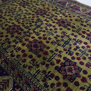 May include: A green rug with a repeating pattern of red, blue, and white geometric shapes. The rug has a border with a similar pattern.