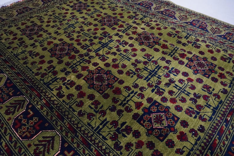 May include: A green rug with a repeating pattern of red, blue, and white geometric shapes. The rug has a border with a similar pattern.