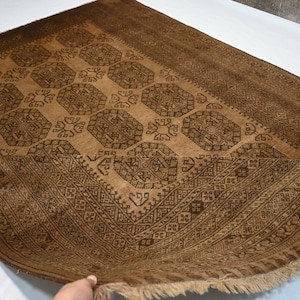 K&ouml;nnte beinhalten: Ein brauner Teppich mit einem geometrischen Muster in einem dunkleren Braunton. Der Teppich hat einen Fransenrand.
