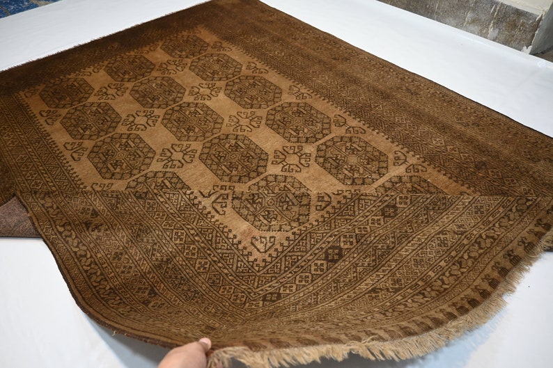 K&ouml;nnte beinhalten: Ein brauner Teppich mit einem geometrischen Muster in einem dunkleren Braunton. Der Teppich hat einen Fransenrand.