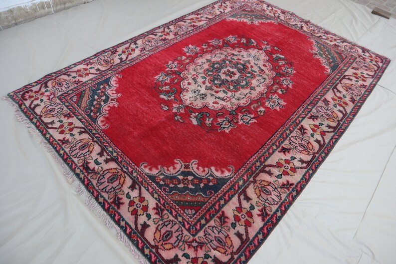 May include: A red rug with a floral pattern and a central medallion. The rug has a pink and black border with intricate details.