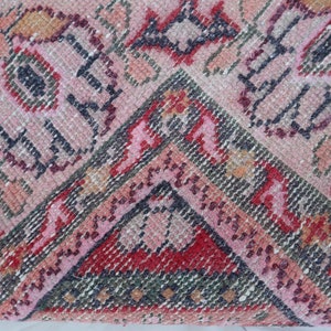 May include: Close-up of a pink, red and green patterned rug with a geometric design. The rug is woven with a variety of textures and colours.