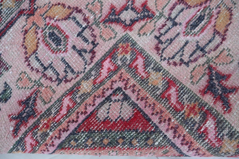 May include: Close-up of a pink, red and green patterned rug with a geometric design. The rug is woven with a variety of textures and colours.