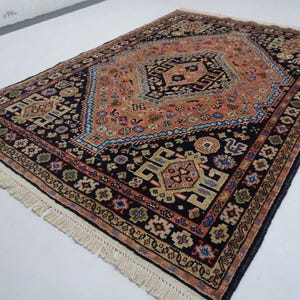 May include: A traditional Persian rug with a black background and intricate floral and geometric patterns in shades of red, orange, blue, and cream. The rug has a fringe border.