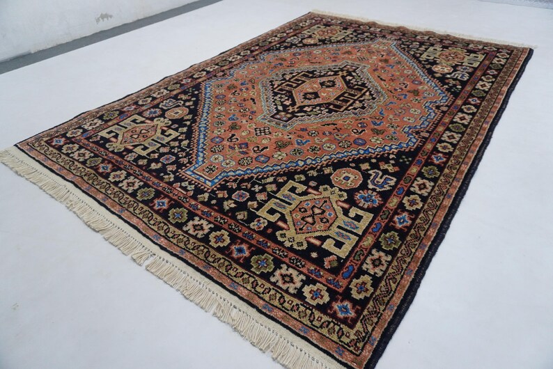 May include: A traditional Persian rug with a black background and intricate floral and geometric patterns in shades of red, orange, blue, and cream. The rug has a fringe border.