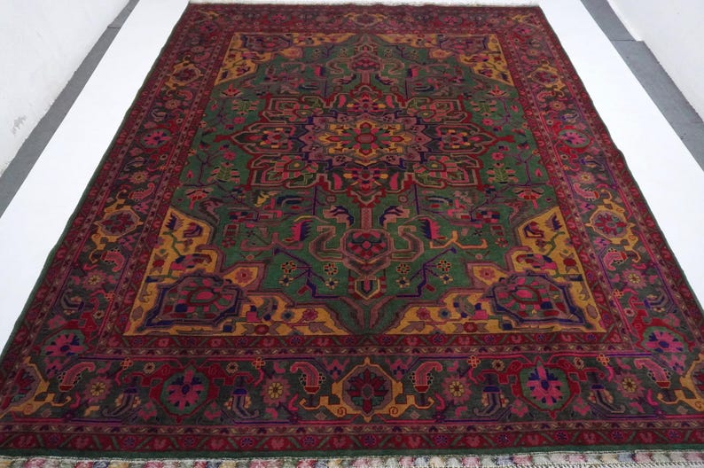 May include: A traditional Persian rug with a green, red and gold colour scheme. The rug features a central medallion with intricate floral and geometric patterns. The rug has a fringed border.