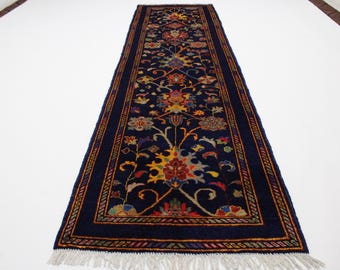 May include: A long, narrow rug with a dark blue background and a colorful floral pattern. The rug has a fringe on both ends.