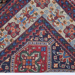 May include: Close-up of a colourful rug with intricate geometric patterns in shades of red, blue, green, and white. The rug has a fringed border.
