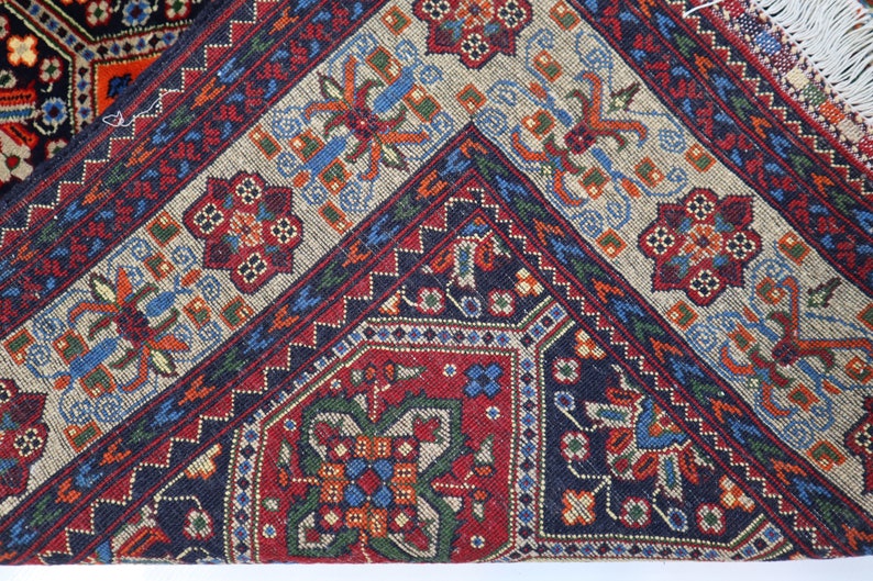 May include: Close-up of a colourful rug with intricate geometric patterns in shades of red, blue, green, and white. The rug has a fringed border.
