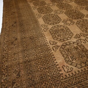 K&ouml;nnte beinhalten: Ein brauner und beiger Teppich mit geometrischem Muster. Der Teppich hat einen dunkelbraunen Rand mit komplizierten Designs.