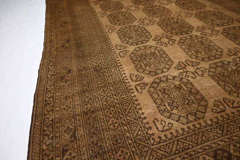 K&ouml;nnte beinhalten: Ein brauner und beiger Teppich mit geometrischem Muster. Der Teppich hat einen dunkelbraunen Rand mit komplizierten Designs.