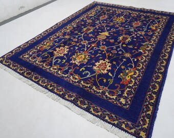 May include: A rectangular, hand-woven rug with a deep blue field and intricate floral patterns in shades of red, yellow, and cream. The rug features a detailed border and fringed edges, showcasing traditional craftsmanship.