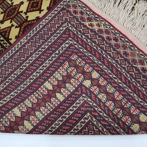 May include: Close-up of a red, white, and blue patterned rug with fringe. The rug has a geometric design with intricate details.