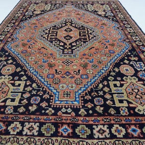 May include: A traditional Persian rug with a dark blue background and intricate patterns in shades of red, orange, blue, and green. The rug features a central medallion with a geometric design and a border with floral motifs.