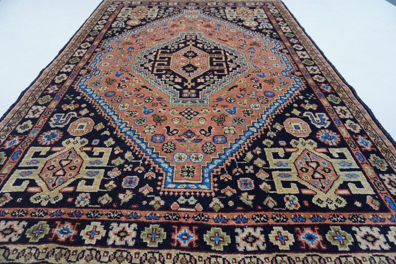 May include: A traditional Persian rug with a dark blue background and intricate patterns in shades of red, orange, blue, and green. The rug features a central medallion with a geometric design and a border with floral motifs.