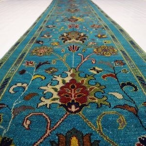 May include: A teal blue runner rug with a floral pattern in shades of red, yellow, green, and brown. The rug has a border with a geometric design.