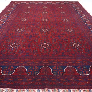 May include: A red rug with a blue and white geometric pattern. The rug has a fringe border.