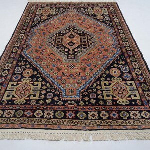 May include: A traditional Persian rug with a black background and intricate patterns in shades of red, orange, blue, and beige. The rug features a central medallion with a diamond shape and a geometric design. The rug has a fringe border.