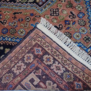 May include: A close-up of a rug with a detailed pattern of blue, red, and white. The rug has a fringe border.