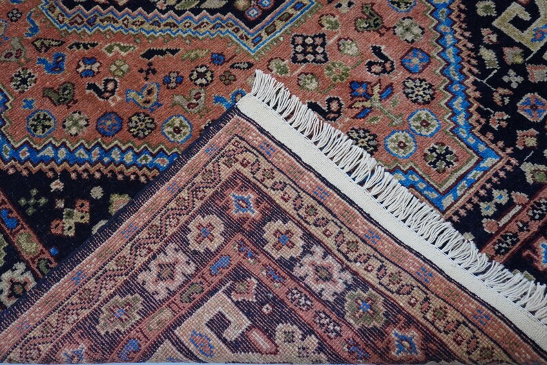 May include: A close-up of a rug with a detailed pattern of blue, red, and white. The rug has a fringe border.