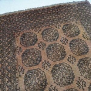 May include: A rectangular, hand-woven rug with a repeating geometric pattern. The rug features a central field of tan with dark brown octagonal medallions and decorative motifs. The border is a darker brown with a repeating geometric design.