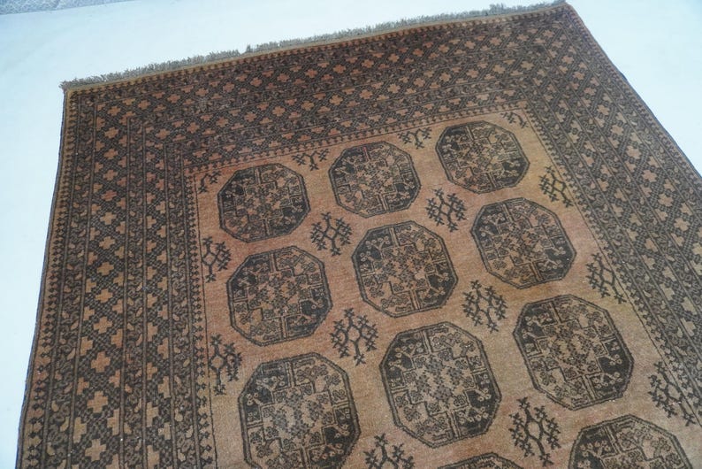 May include: A rectangular, hand-woven rug with a repeating geometric pattern. The rug features a central field of tan with dark brown octagonal medallions and decorative motifs. The border is a darker brown with a repeating geometric design.