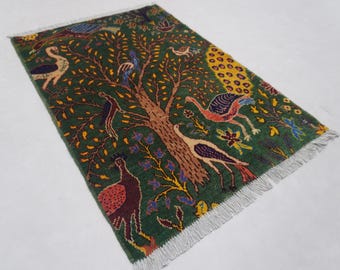 May include: Rectangular green rug with a tree and bird design. The rug features a central brown tree with yellow leaves, surrounded by various birds in shades of red, white, and blue. The rug has a fringe on the edges.