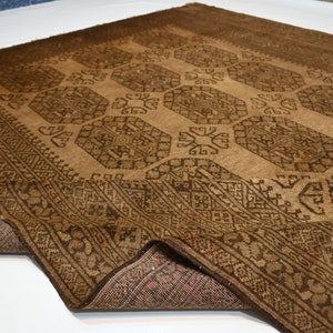 K&ouml;nnte beinhalten: Ein brauner und schwarzer Teppich mit geometrischem Muster. Der Teppich ist in der Mitte gefaltet und die Unterseite ist sichtbar.