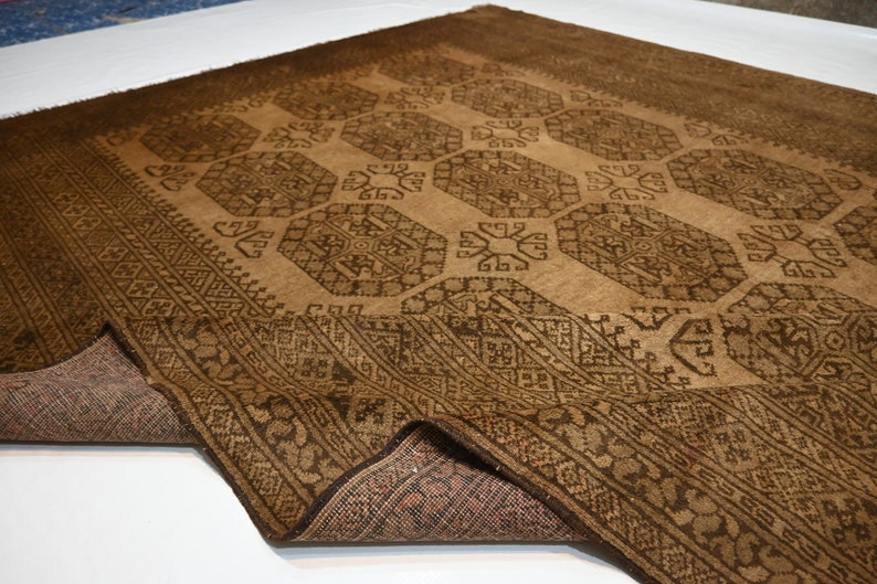 K&ouml;nnte beinhalten: Ein brauner und schwarzer Teppich mit geometrischem Muster. Der Teppich ist in der Mitte gefaltet und die Unterseite ist sichtbar.