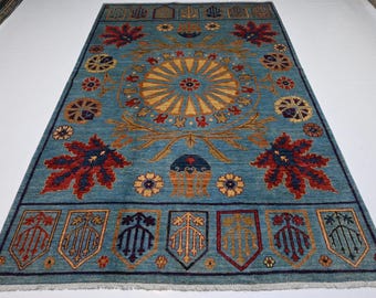 May include: A rectangular, turquoise rug with an intricate floral design. The central motif is a sunburst in yellow and gold, surrounded by red and blue leaf-like shapes and floral patterns. The rug's border features shield-like designs.