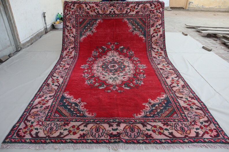 May include: A red rug with a floral pattern and a central medallion. The rug has a fringe border and is made of wool.