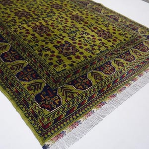 May include: A green rug with a traditional Persian design. The rug has a dark blue border with red and yellow accents. The rug has a fringe on all sides.