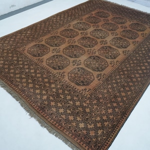 May include: A rectangular, brown rug with a central pattern of repeating octagons. The rug has a dark brown border with a geometric design and fringed edges. The color palette is primarily brown and tan, creating a warm, inviting aesthetic.