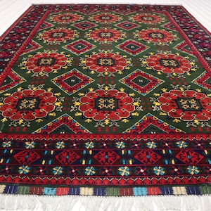 Puede incluir: Una alfombra persa tradicional con fondo verde y intrincados patrones florales rojos, amarillos y azules. La alfombra tiene un borde azul oscuro con un diseño geométrico repetitivo.