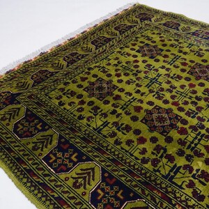 May include: A green rug with a traditional Persian design. The rug has a dark blue border with red and white accents. The center of the rug features a repeating pattern of geometric shapes and floral motifs.