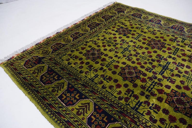 May include: A green rug with a traditional Persian design. The rug has a dark blue border with red and white accents. The center of the rug features a repeating pattern of geometric shapes and floral motifs.