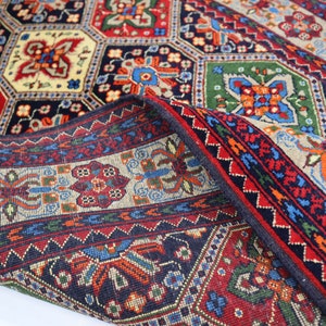 May include: A traditional Persian rug with a colourful geometric pattern. The rug is folded in half, revealing the intricate details of the design. The colours include red, blue, green, and cream.