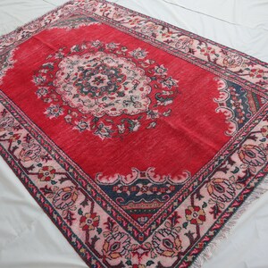 May include: A red rug with a floral pattern in shades of pink, blue, and green. The rug has a central medallion with a repeating pattern of flowers and leaves. The rug has a fringed border.