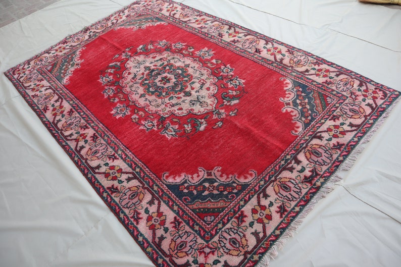 May include: A red rug with a floral pattern in shades of pink, blue, and green. The rug has a central medallion with a repeating pattern of flowers and leaves. The rug has a fringed border.