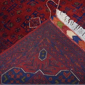 Pu&ograve; includere: Primo piano di un tappeto rosso e blu con frange bianche. Il tappeto presenta un design tradizionale con dettagli intricati.