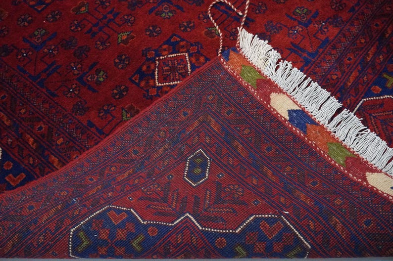 Pu&ograve; includere: Primo piano di un tappeto rosso e blu con frange bianche. Il tappeto presenta un design tradizionale con dettagli intricati.