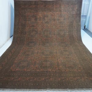 May include: A large, rectangular rug with a detailed, repeating geometric pattern in shades of brown, rust, and olive green. The rug has a fringe along the bottom edge and is displayed against a white background.