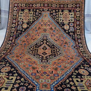 May include: A traditional Persian rug with a black background and a central medallion in shades of pink, blue, and beige. The rug features intricate geometric patterns and floral motifs.