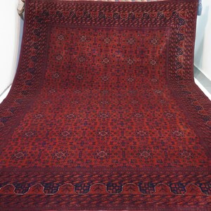 May include: A large, red rug with a detailed, intricate pattern. The rug has a dark blue border with a repeating design.