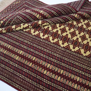 May include: A traditional style rug with a cream background and intricate red, black, and yellow geometric patterns. The rug has a fringe border.