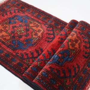 May include: A red, blue, and green patterned rug with a fringed edge. The rug is folded in half and has a traditional design.