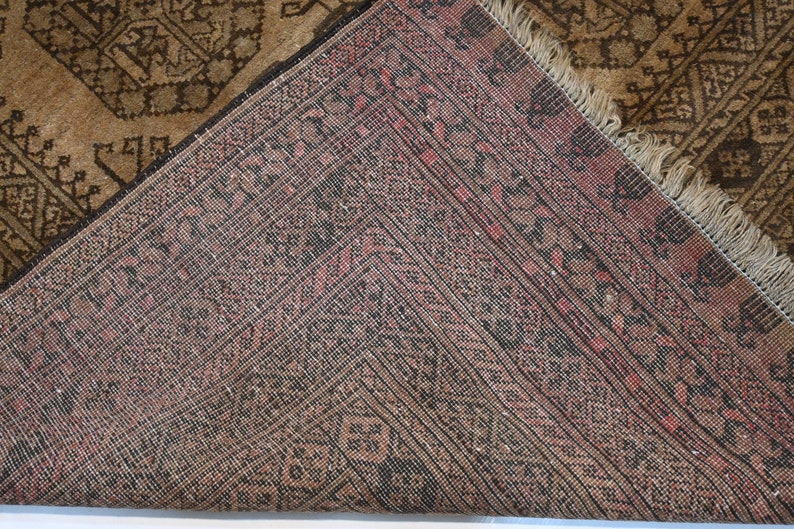 K&ouml;nnte beinhalten: Nahaufnahme der R&uuml;ckseite eines braunen und roten Teppichs mit Fransenrand. Der Teppich hat ein geometrisches Muster.