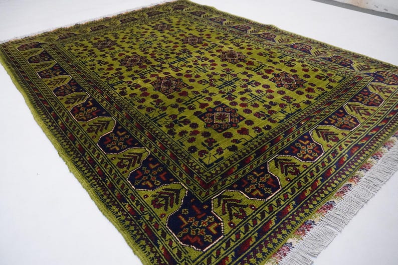 May include: A green rug with a traditional Persian design. The rug has a dark blue and red border with a repeating pattern of flowers and leaves. The center of the rug features a large, intricate design with a geometric pattern.