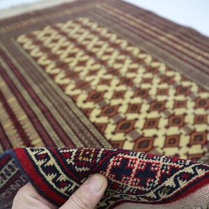 May include: A traditional hand-woven rug with a geometric pattern in shades of red, brown, beige, and cream. The rug has a fringe border and is made of wool.